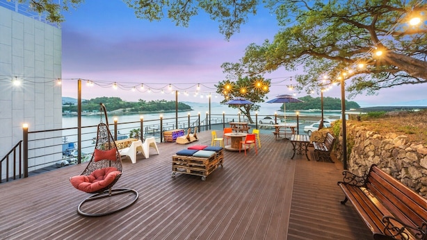 Eine Terrasse mit Sitzgelegenheiten, Lichterketten und Blick auf einen Fluss und Hügel.