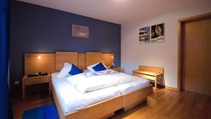 A bedroom with a wooden bed, two bedside tables, a nightstand, and a blue wall. - Gästehaus Im Tal 18 (Hellenthal)
