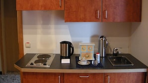 A compact kitchen with wooden cabinets, a coffee maker, a kettle, a small table with a teapot, and a sink. - Gästehaus Im Tal 18 (Hellenthal)