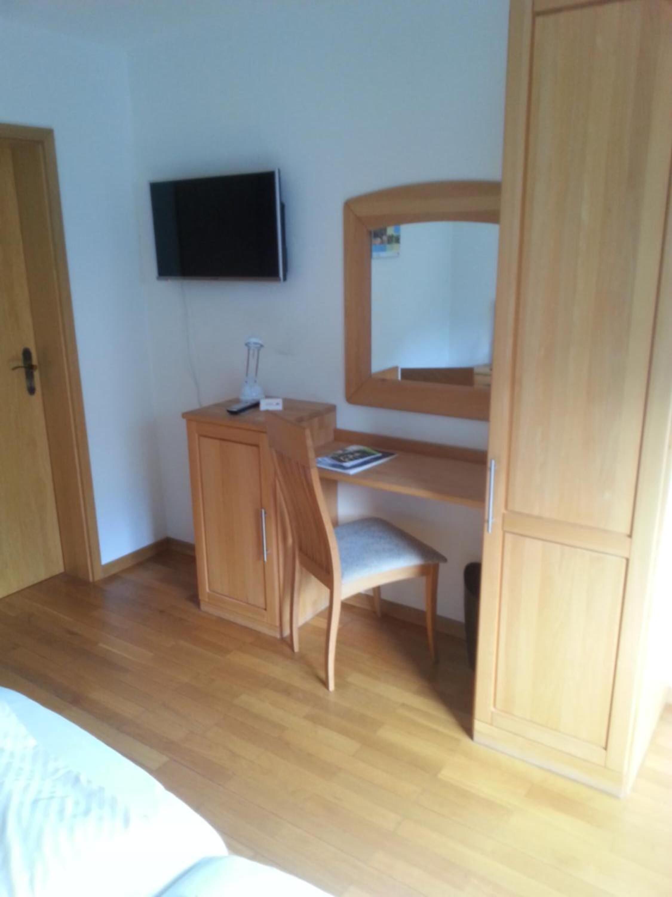 A bedroom with a wooden desk, chair, and a television mounted on the wall.