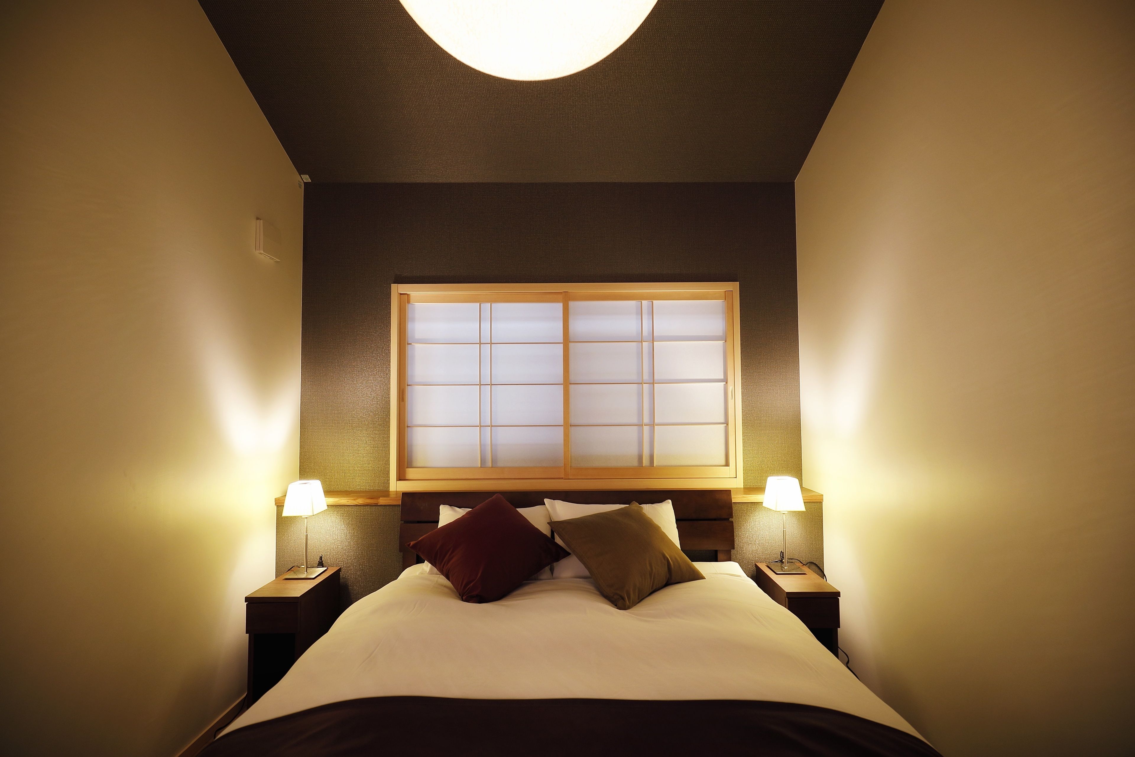 A neatly made bed with a headboard, two bedside lamps, and a window with frosted glass panels.