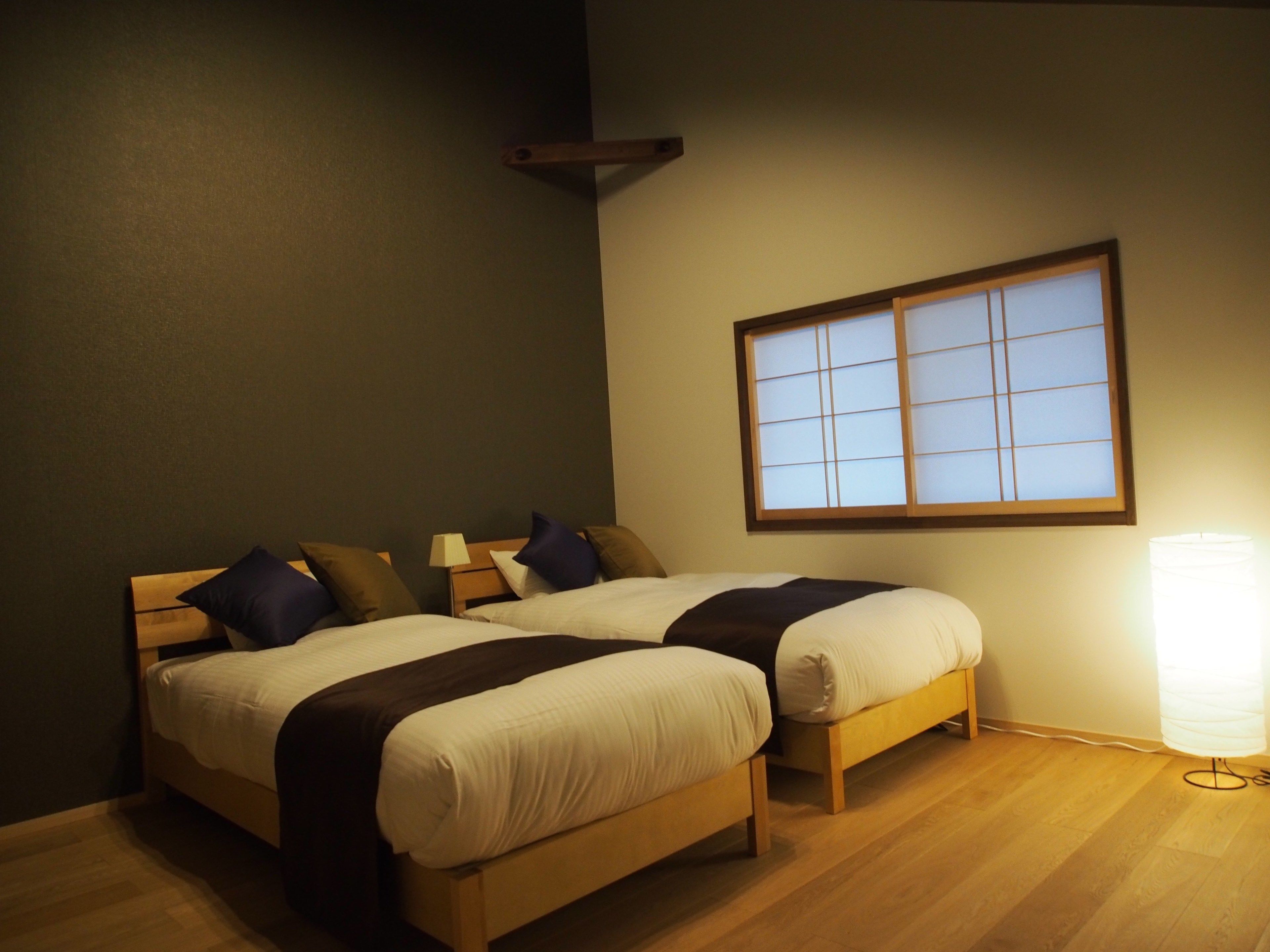 A room with two beds, a window, and a lamp.