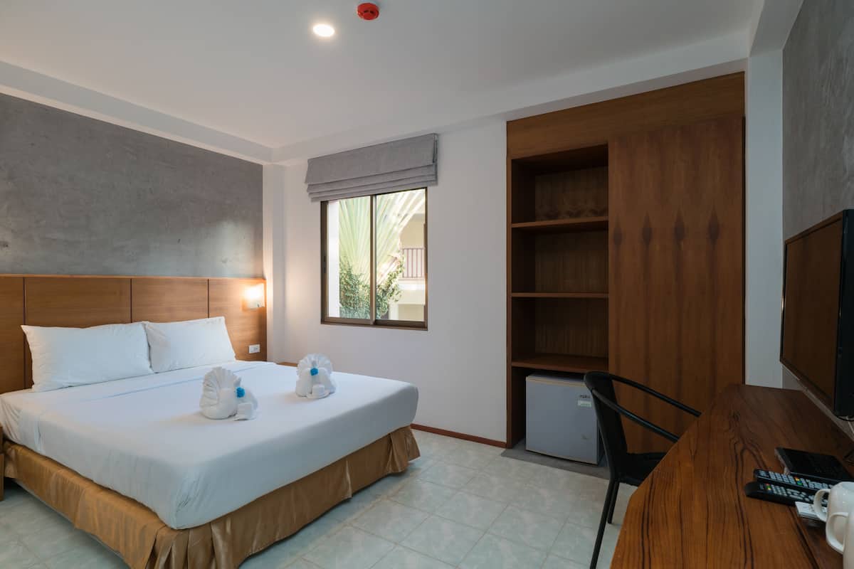 A hotel room with a large bed, a desk with a computer, a TV, and a small refrigerator.