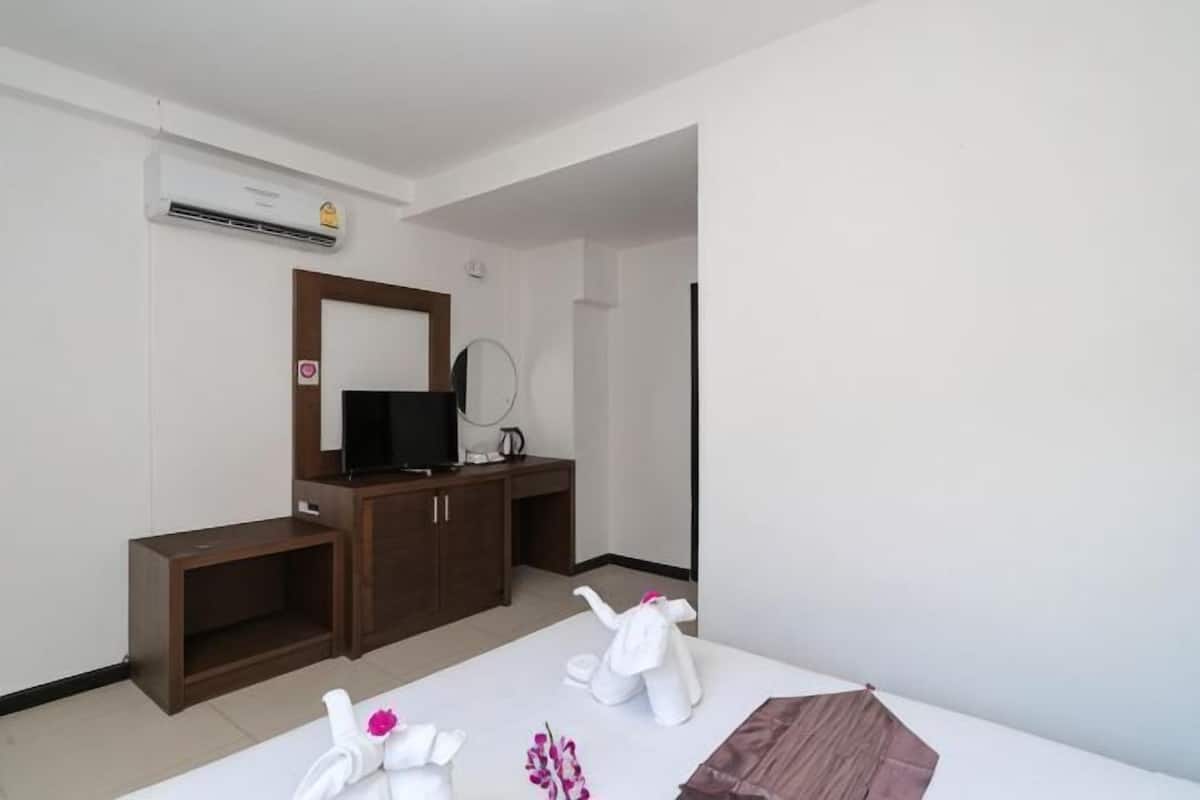 A hotel room with a TV, wooden furniture, a mirror, and a white bed.
