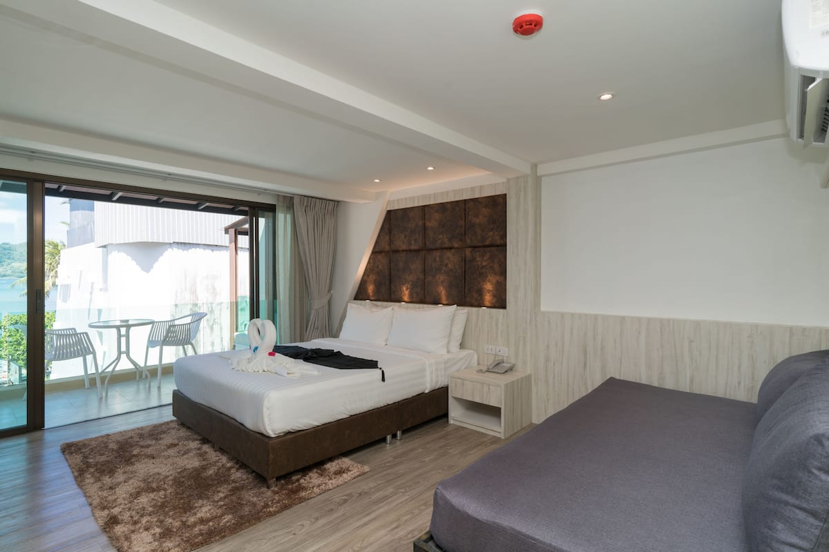 A modern hotel room with a large bed, a bedside table with a phone, a small desk, and a view of the outdoors through a sliding glass door.