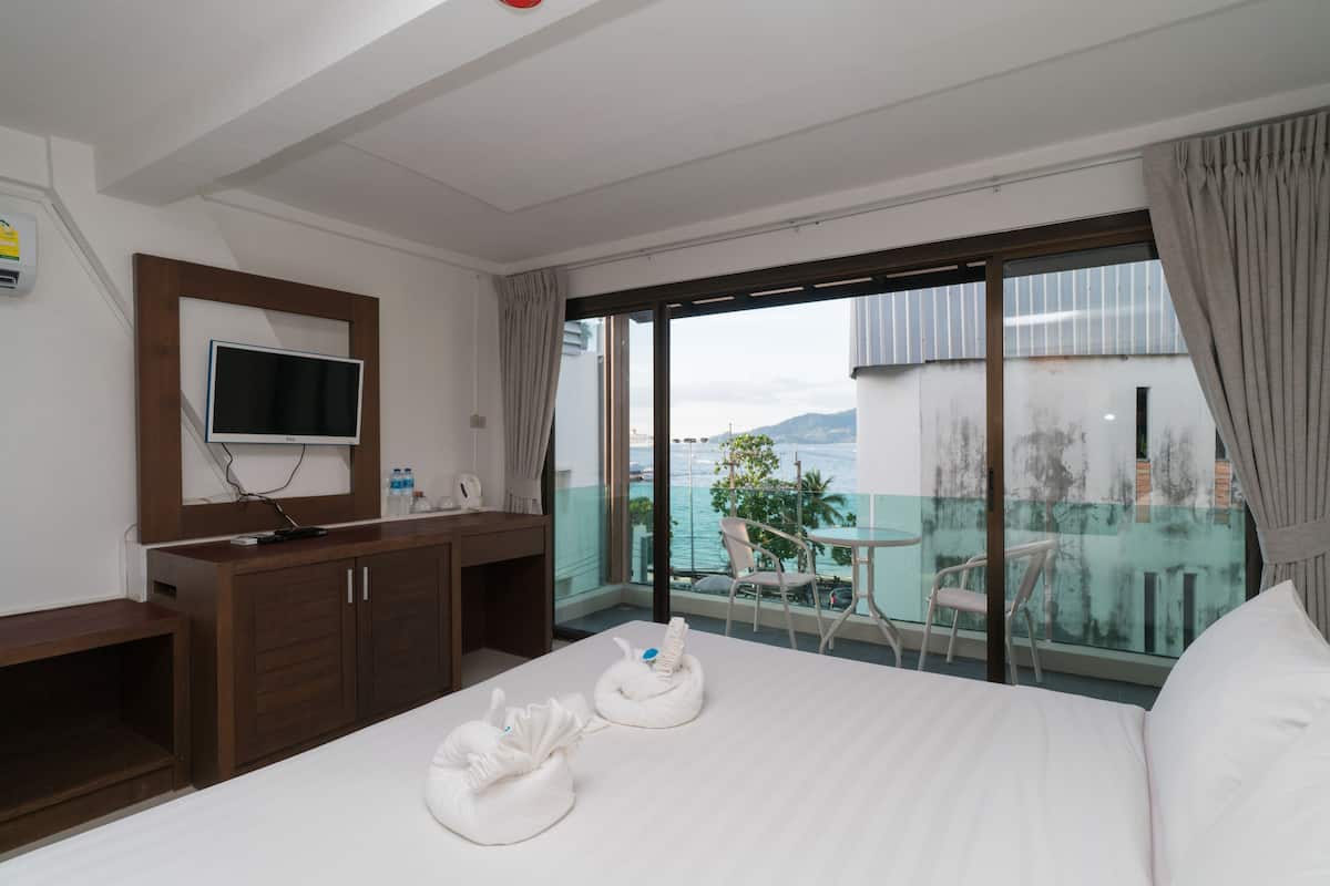 A hotel room with a bed, a TV, a desk, and a balcony with a view of the sea.