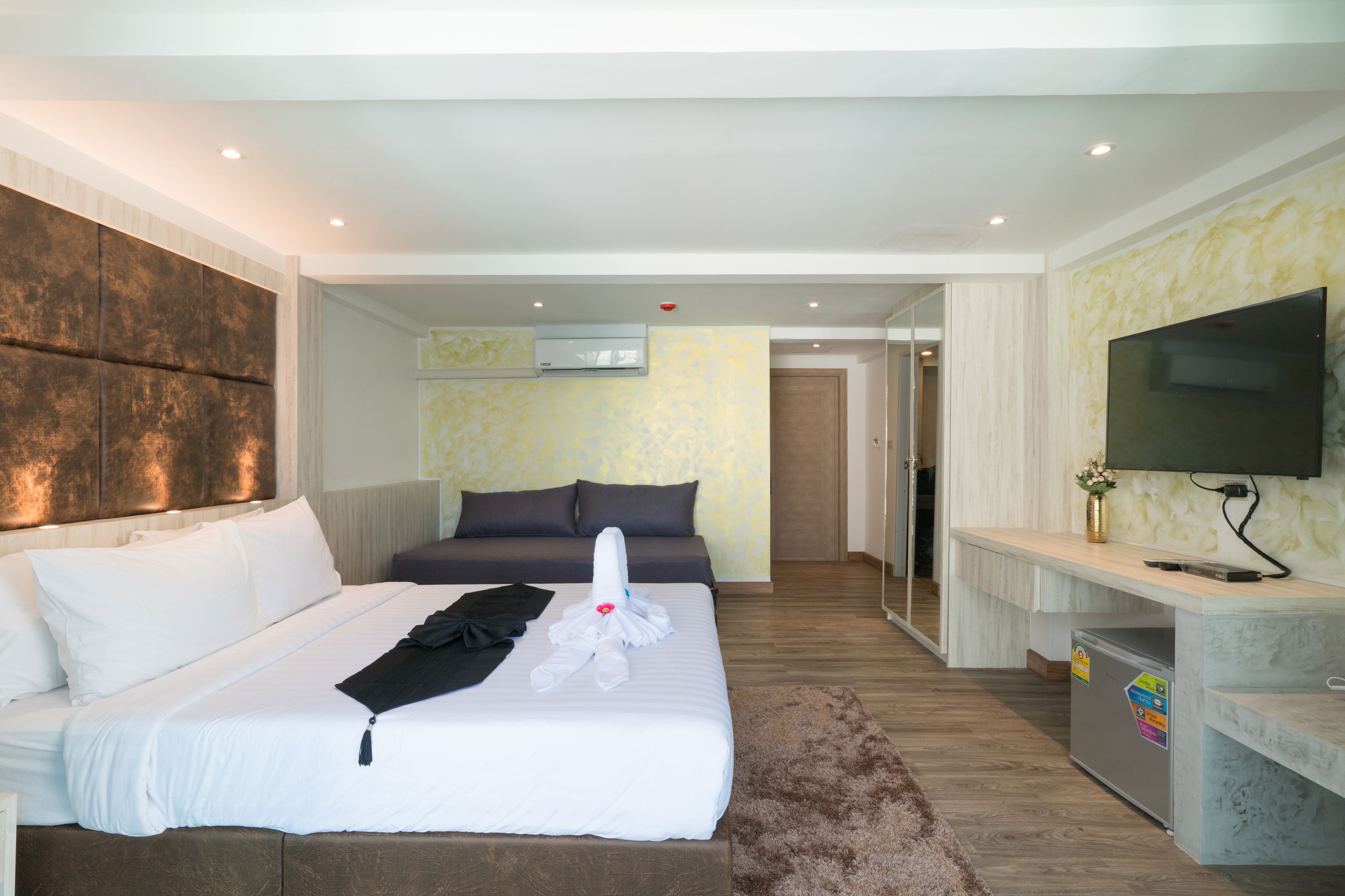 A hotel room with a large bed, a TV, a desk, and a small fridge.