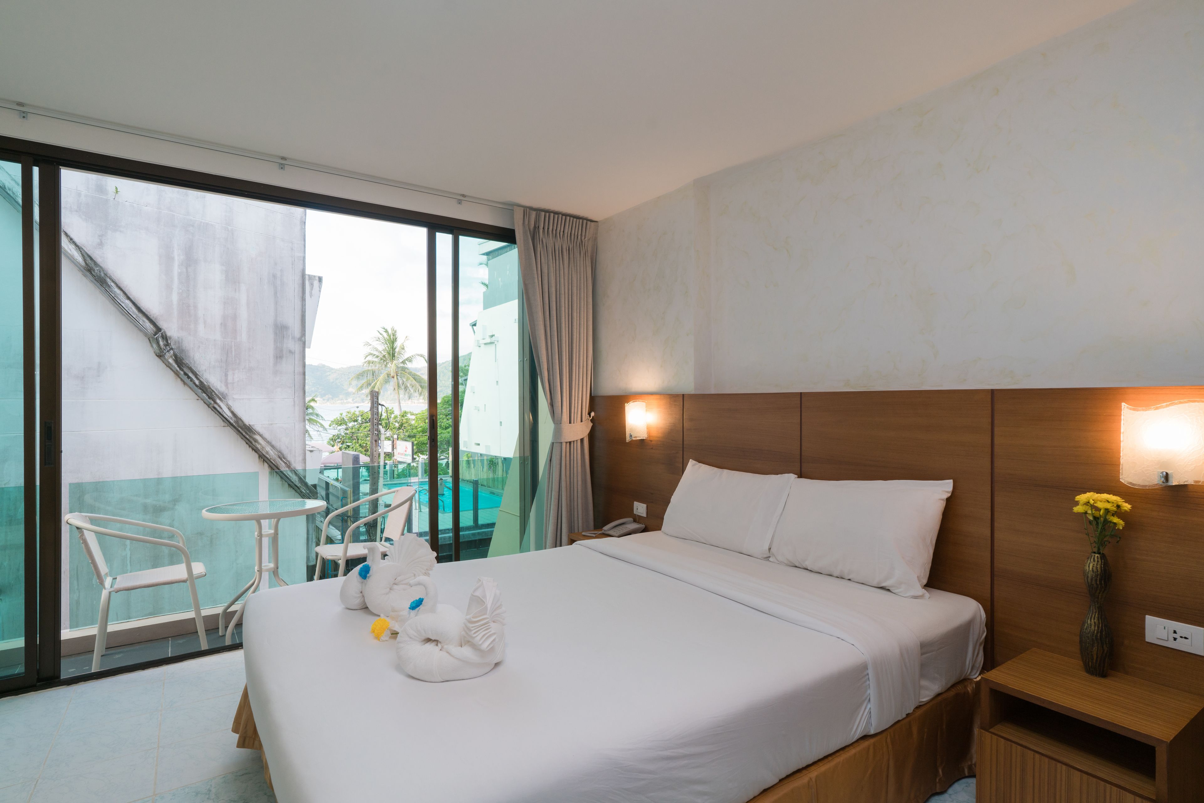 Ein Hotelzimmer mit einem großen Bett, einem Holz-Kopfteil, einem Nachttisch mit einer Vase, einem Balkon mit einer Glastür und einem Sessel.
