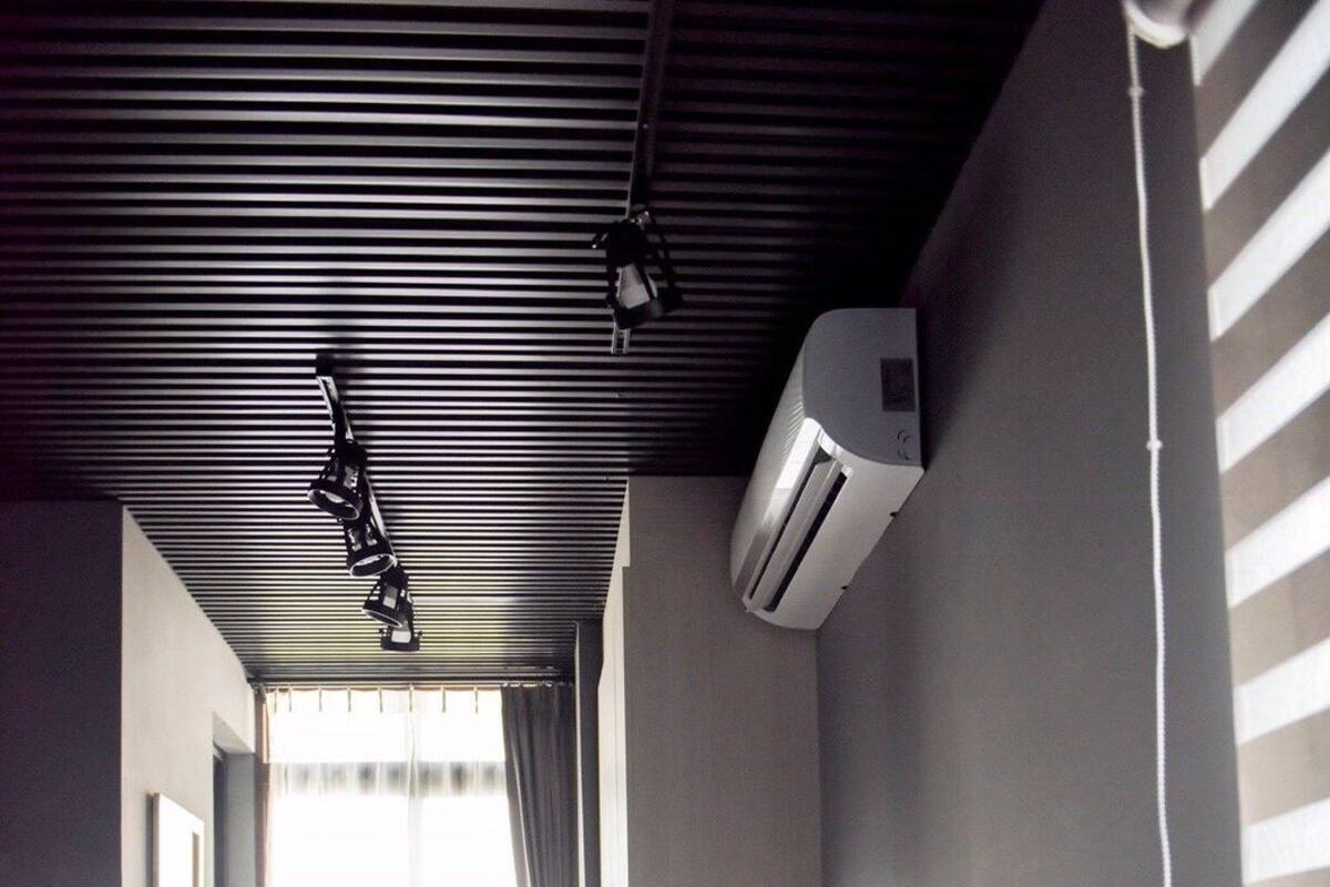 A hotel room with a bed, a bedside table, a mirror, a window with curtains, an air conditioning unit, and a wall-mounted phone.