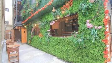 A building with a vertical garden facade, wooden benches, and a window with hanging lights.