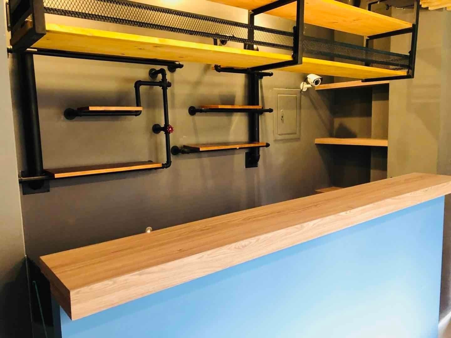 A bunk bed with a wooden frame and metal mesh top, a desk with a blue surface, and a wall-mounted shelf with a camera.