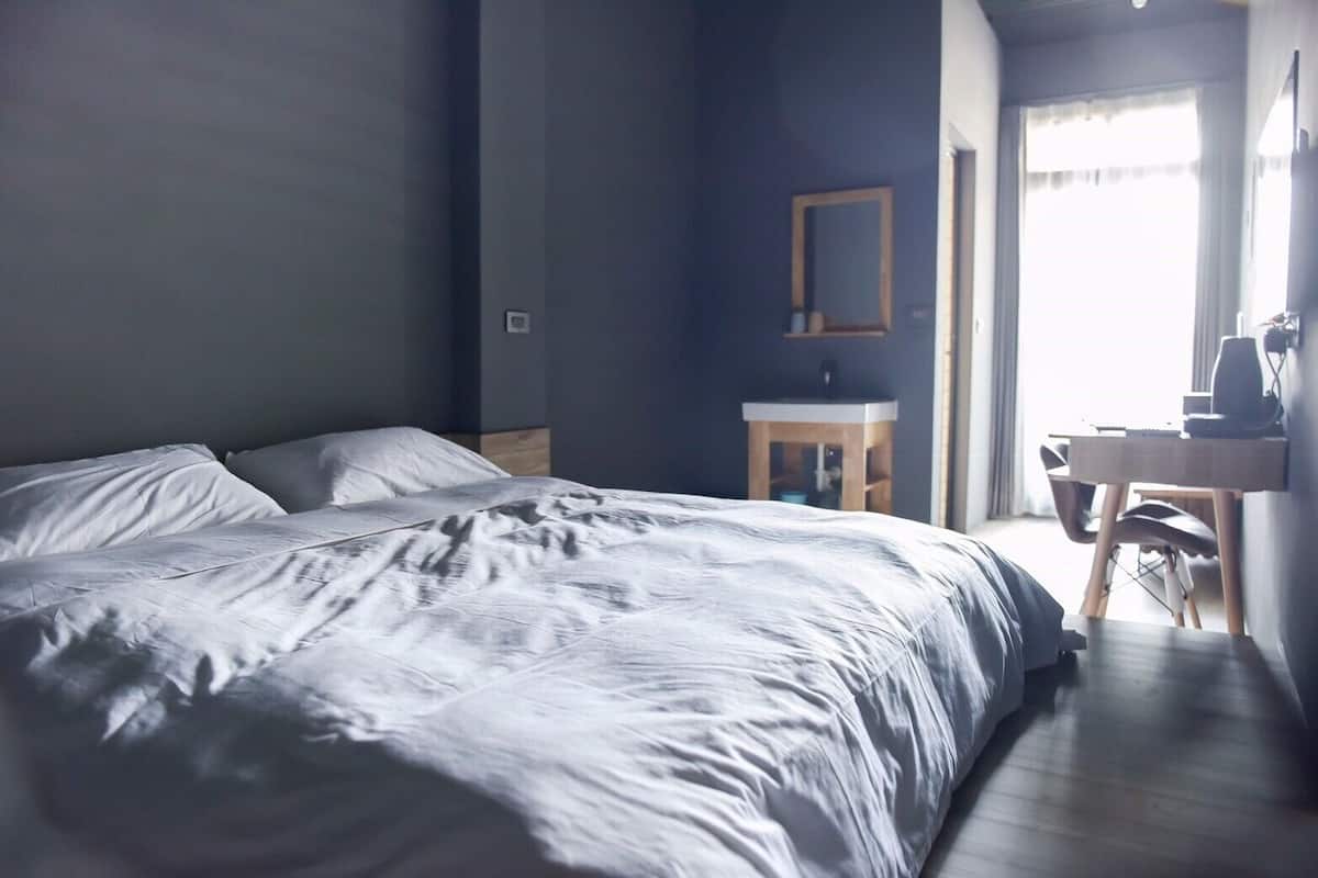A bedroom with a large bed, a small bedside table, a mirror, and a desk with a chair.