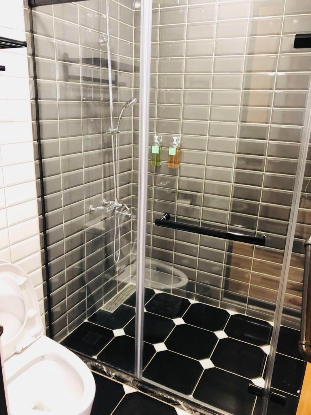 A shower stall with a glass door, a black and white tiled floor, and a toilet to the left.