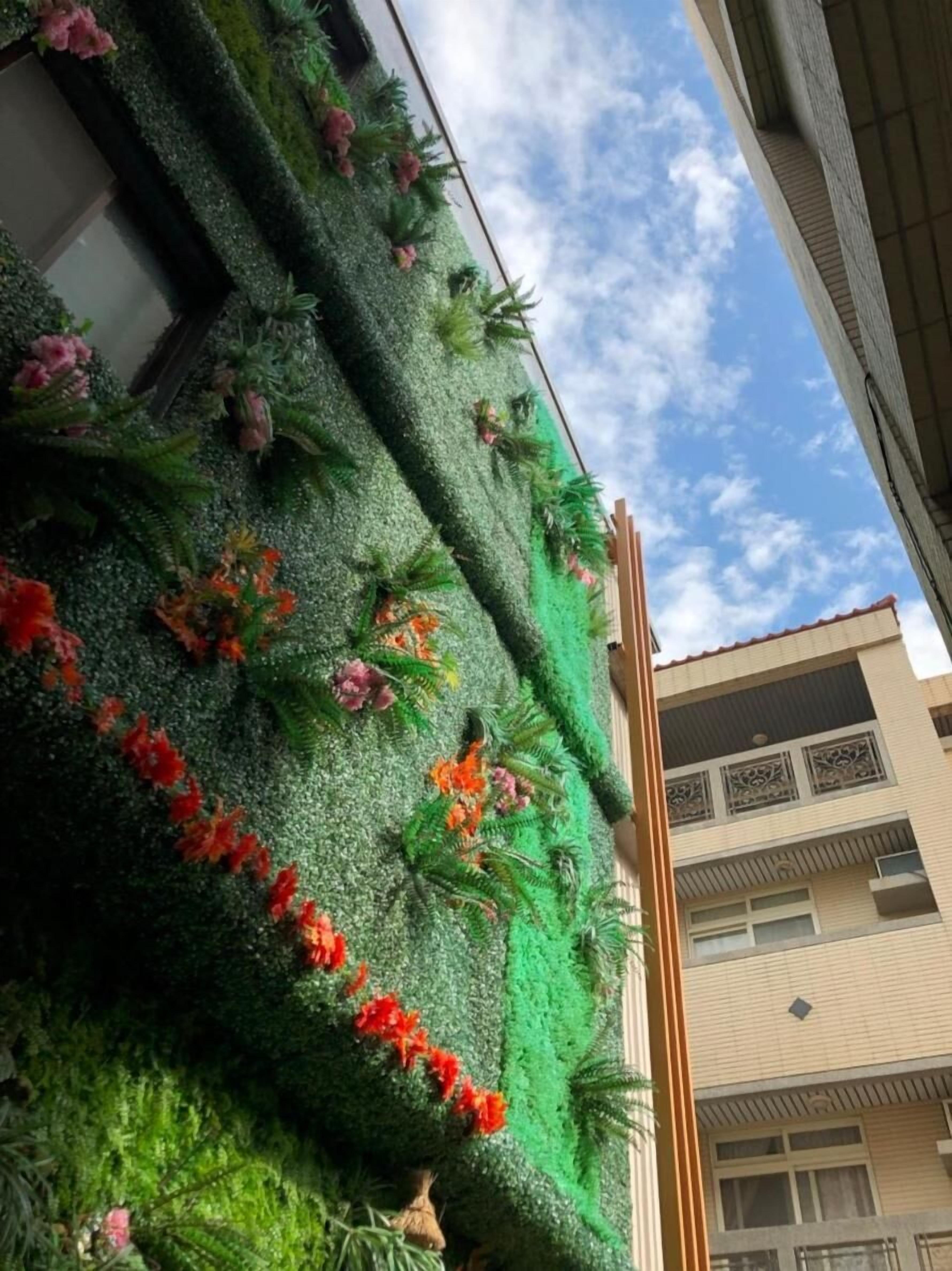 Fachada de edificio con jardín vertical verde y flores rojas.
