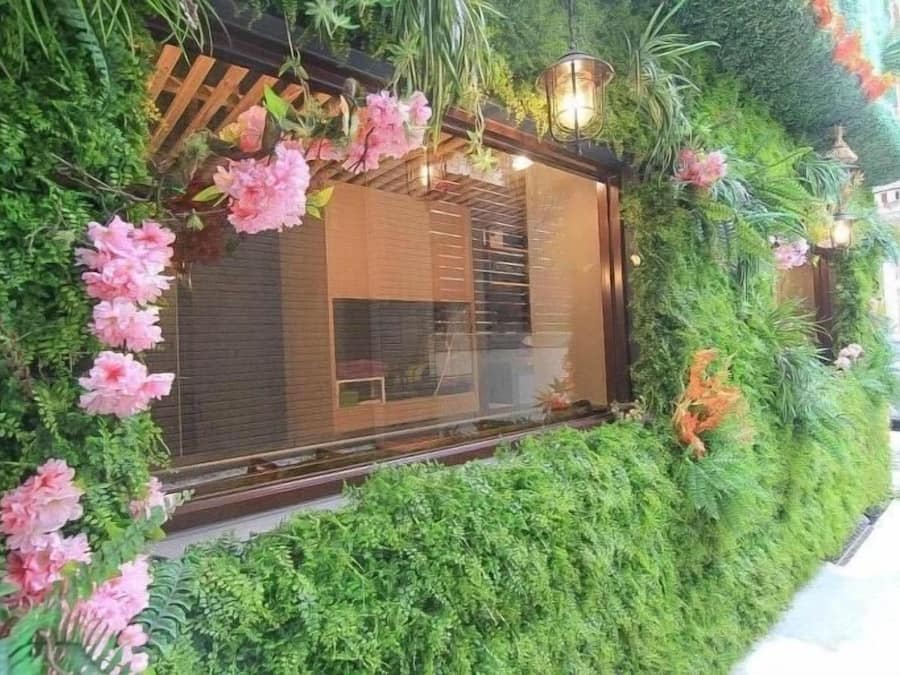 A modern building with a large window, surrounded by lush greenery and pink flowers.