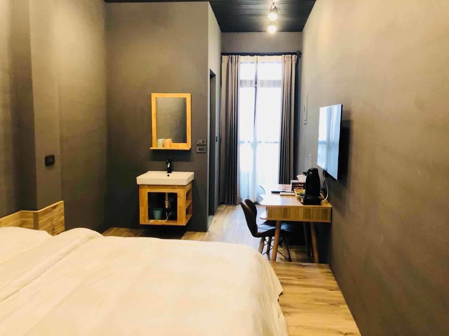 A hotel room with a bed, a desk with a chair, a television, a small cabinet with a mirror, and a window with curtains.