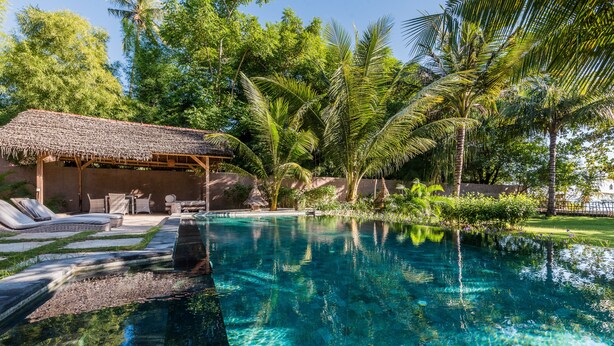 A clear swimming pool with lounge chairs and a thatched-roof structure.