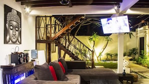 Una sala de estar moderna con sofá, mesa de centro, televisor y una escalera que conduce a un área exterior con plantas.