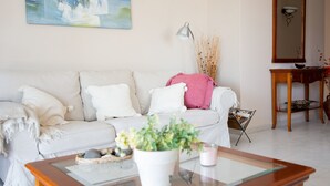 A living room with a white sofa, a glass coffee table with a vase of flowers, a lamp, and a mirror.