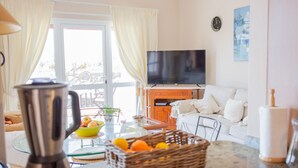 A modern living room with a television, white sofa, and a glass coffee table with fruit.