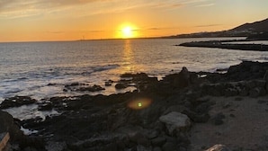 A sunset over a rocky coastline with a clear sky.