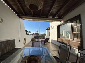 Un espace extérieur abrité, avec une table en verre, des chaises et un panier en osier.