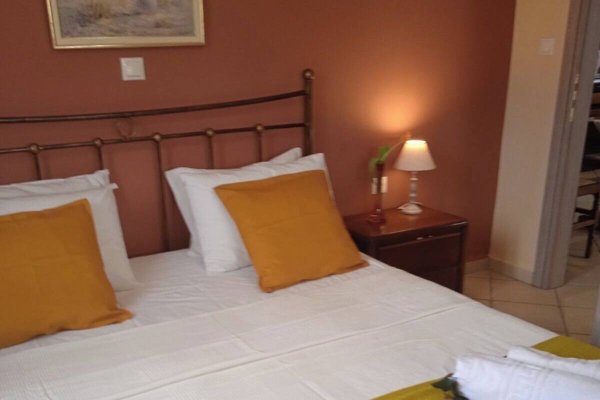 Un lit bien fait, avec du linge de lit blanc et deux coussins orange, une lampe de chevet et un tableau accroché au mur.