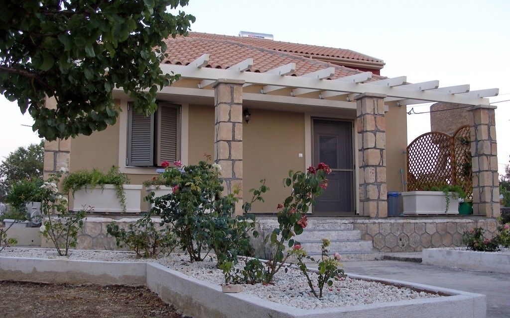 Ett hus med en fasad av sten, ett tak täckt med takpannor och en inglasad veranda med en pergola.