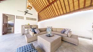 A spacious living area with a high ceiling, woven ceiling, and a ceiling fan. There are two sofas with cushions and a coffee table with a candle. - Jambu Villa Lombok (Tanjung)