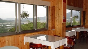 Un restaurante con paredes de madera y ventanas amplias que ofrecen vistas a un paisaje montañoso. Las mesas están dispuestas con manteles blancos y sillas de madera.