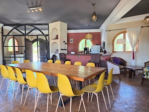 Un coin repas avec une grande table en bois et des chaises jaunes, une cuisine en arrière-plan et un bar avec un lampadaire.