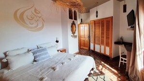 Un dormitorio con cama, lámpara colgante de fibras naturales, armario de madera y televisor sobre un mueble.