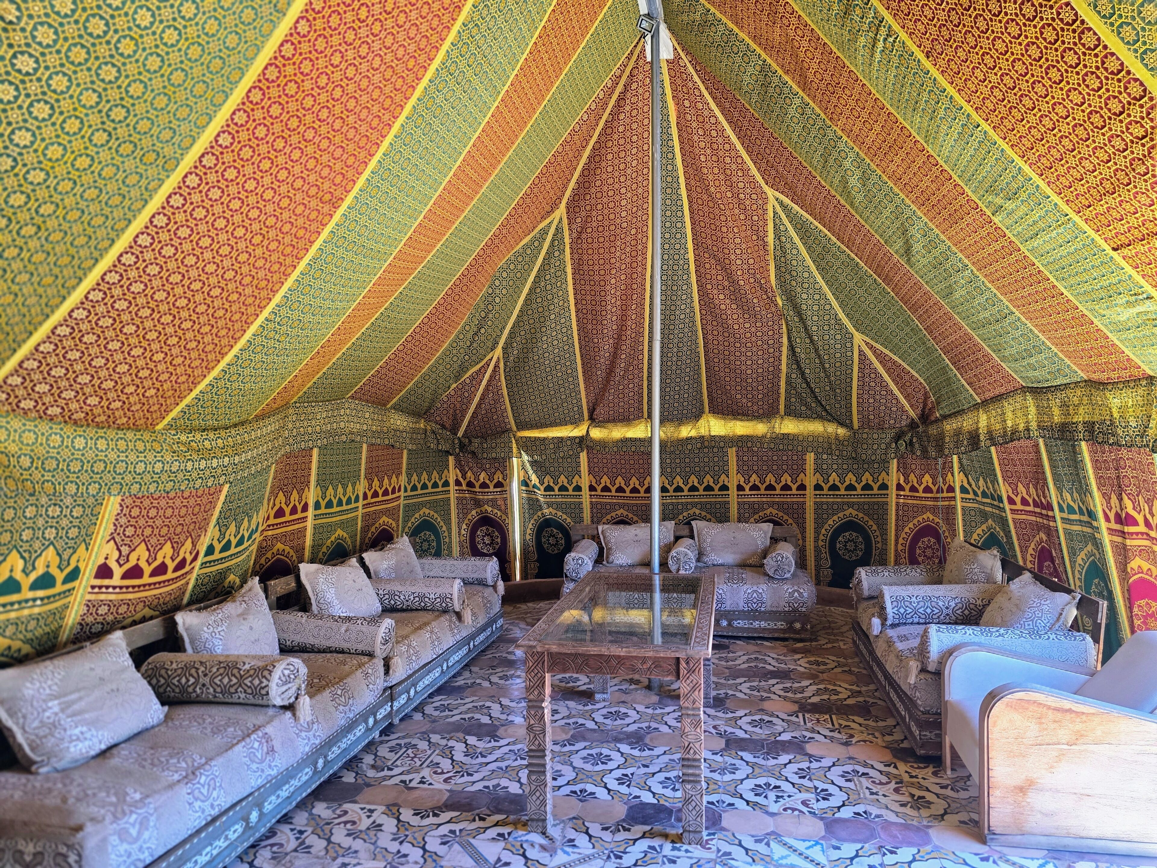 Een tent met wanden van patroonweefsel, een centrale glazen tafel en kussens met een patroon.