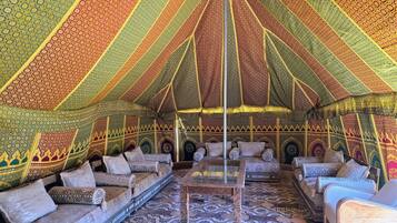 Een tent met wanden van patroonweefsel, een centrale glazen tafel en kussens met een patroon.