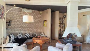 Una sala de estar con pared de ladrillo, una mesa redonda de madera, un sofá con cojines estampados y una lámpara moderna.