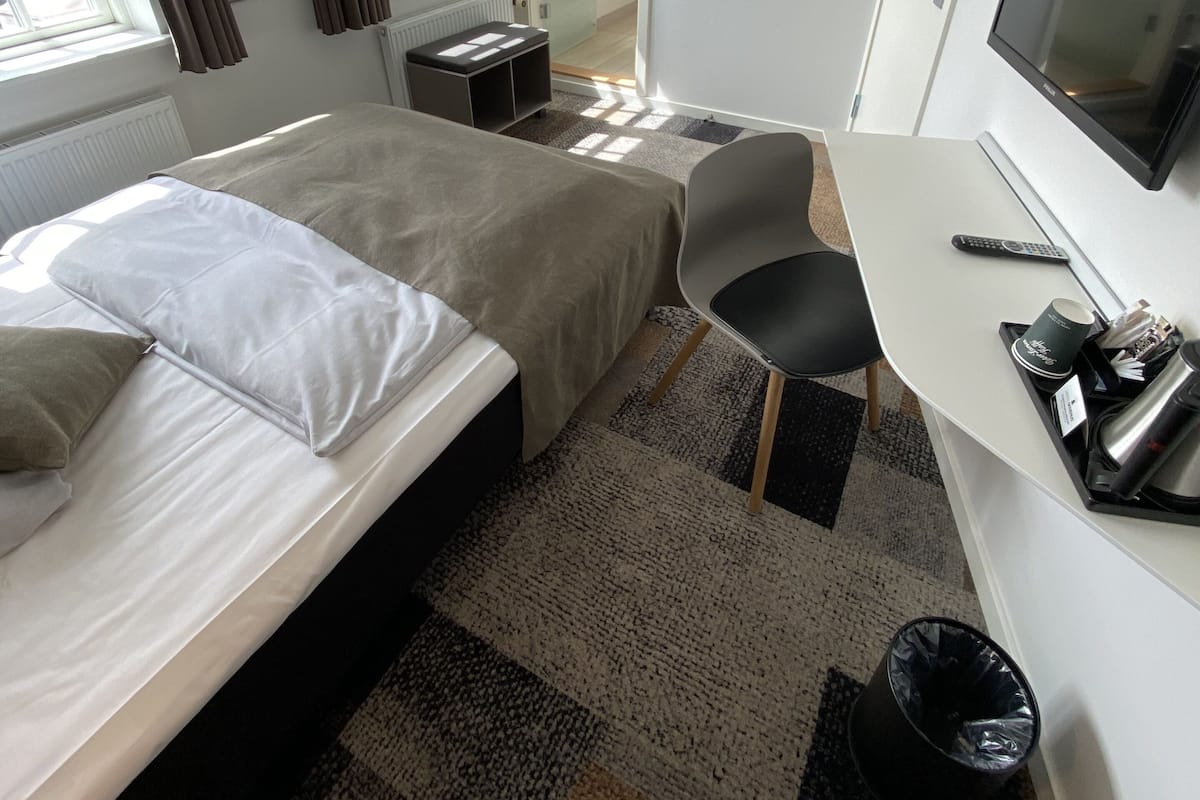 Habitación de hotel con cama, escritorio, silla, televisor y ventana con cortinas.
