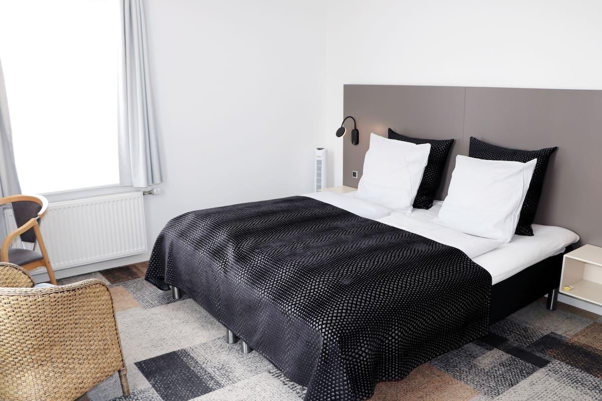 Una habitación de hotel moderna con una cama grande, una mesita de noche, una lámpara y una silla.