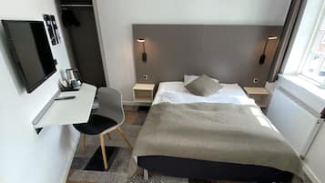 Una habitación de hotel moderna con una cama, mesitas de noche, un escritorio con una silla, un televisor y una ventana.