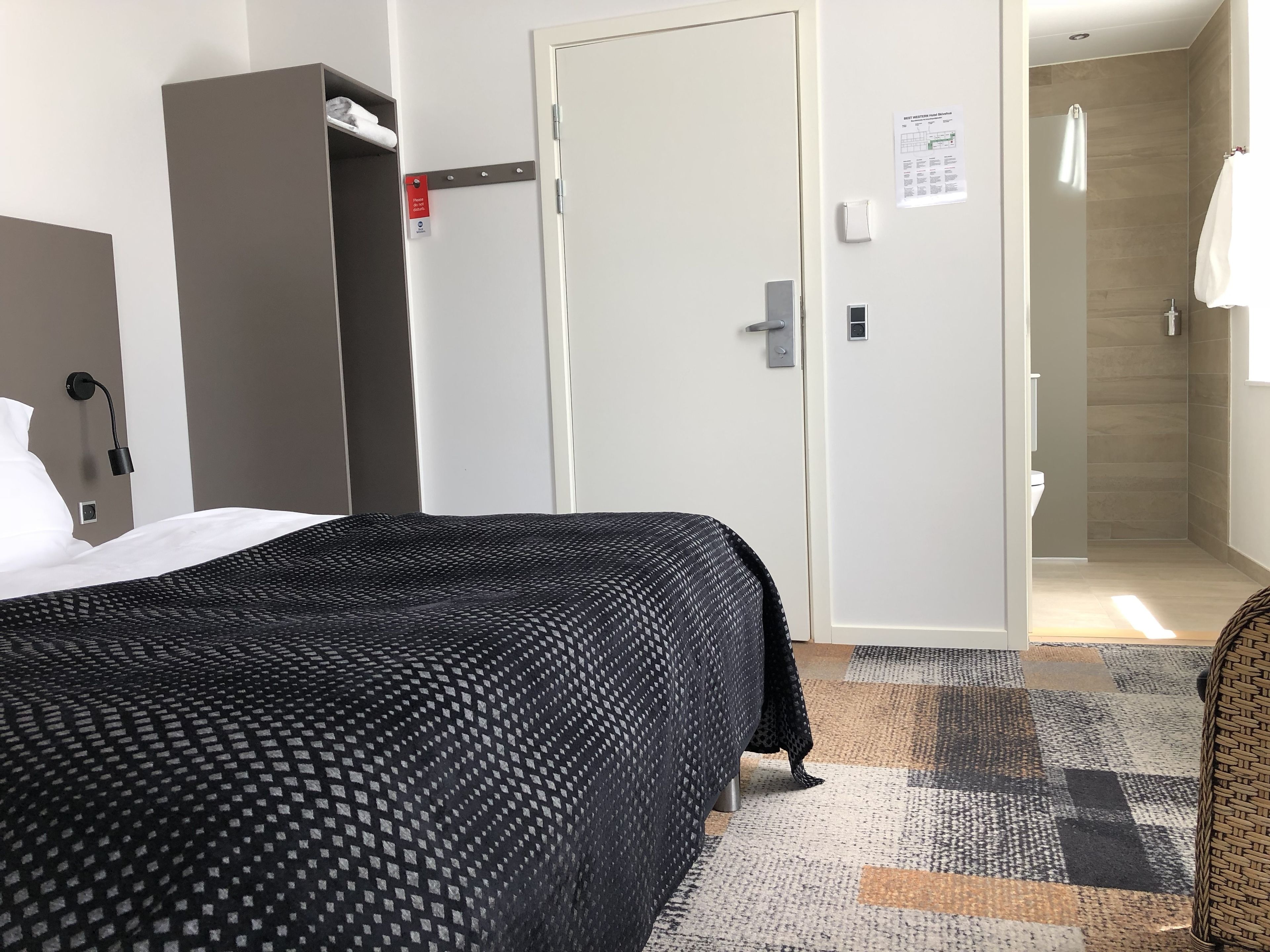 Habitación de hotel con cama, armario, una puerta y un baño visible a través de otra puerta abierta.
