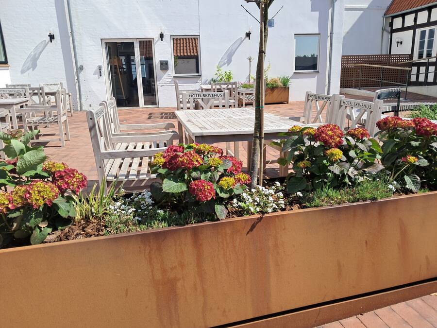 An outdoor seating area with wooden furniture and a planter with hydrangeas.