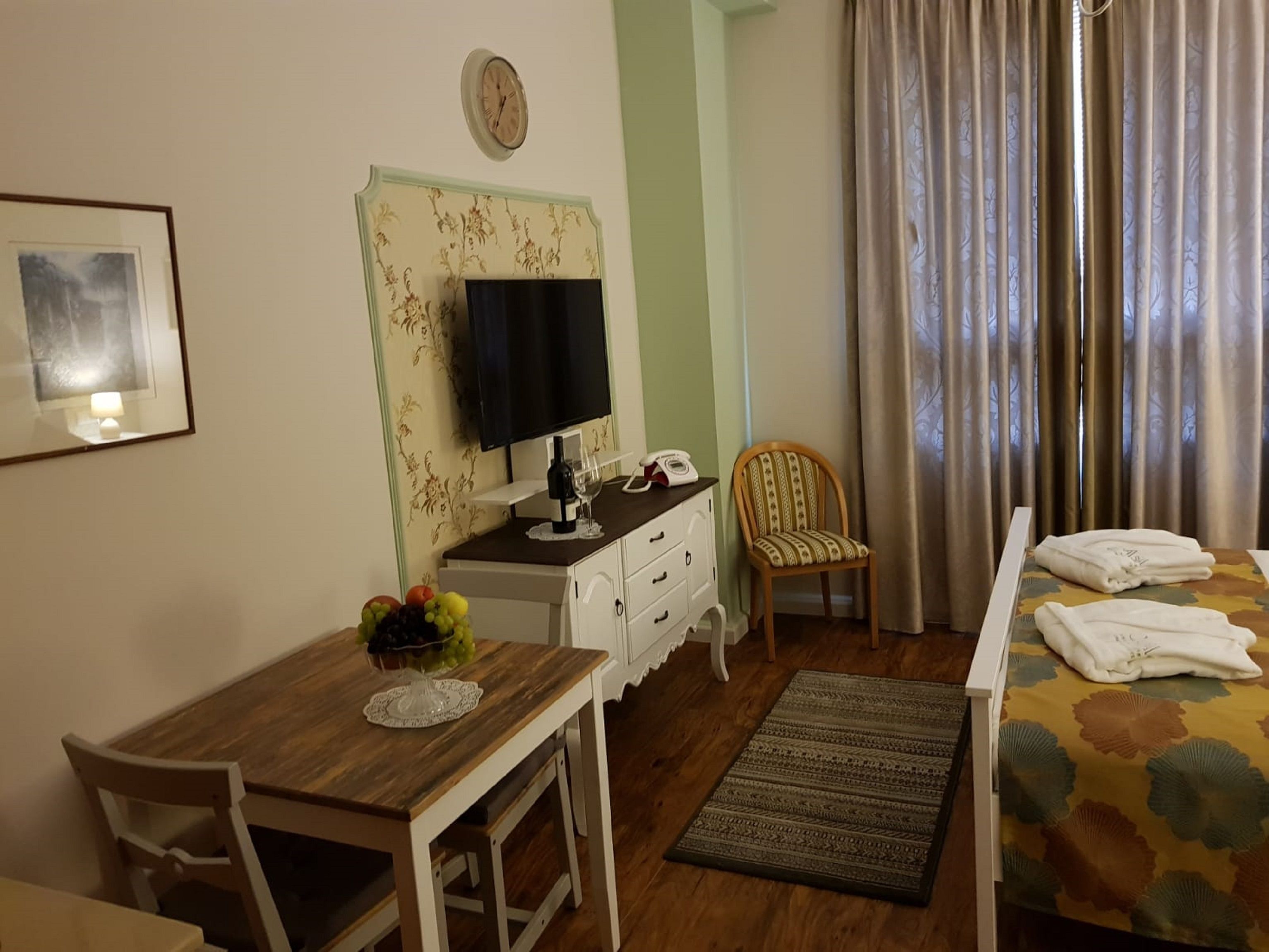 A hotel room with a wooden desk, a television, a chair, a bed with towels, and a patterned rug.