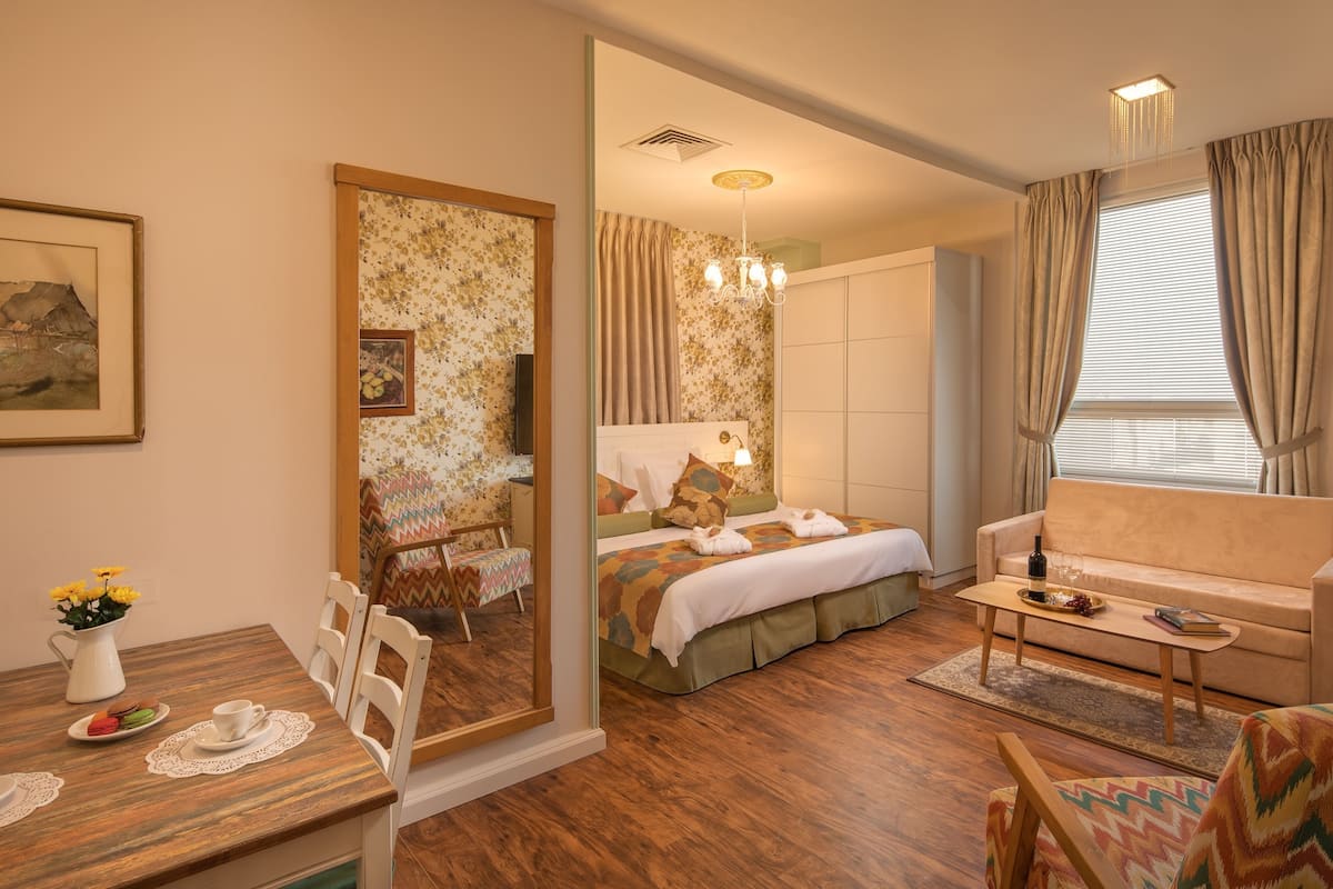 Habitación de hotel con cama, sofá, zona de comedor con mesa y sillas, y un espejo grande.