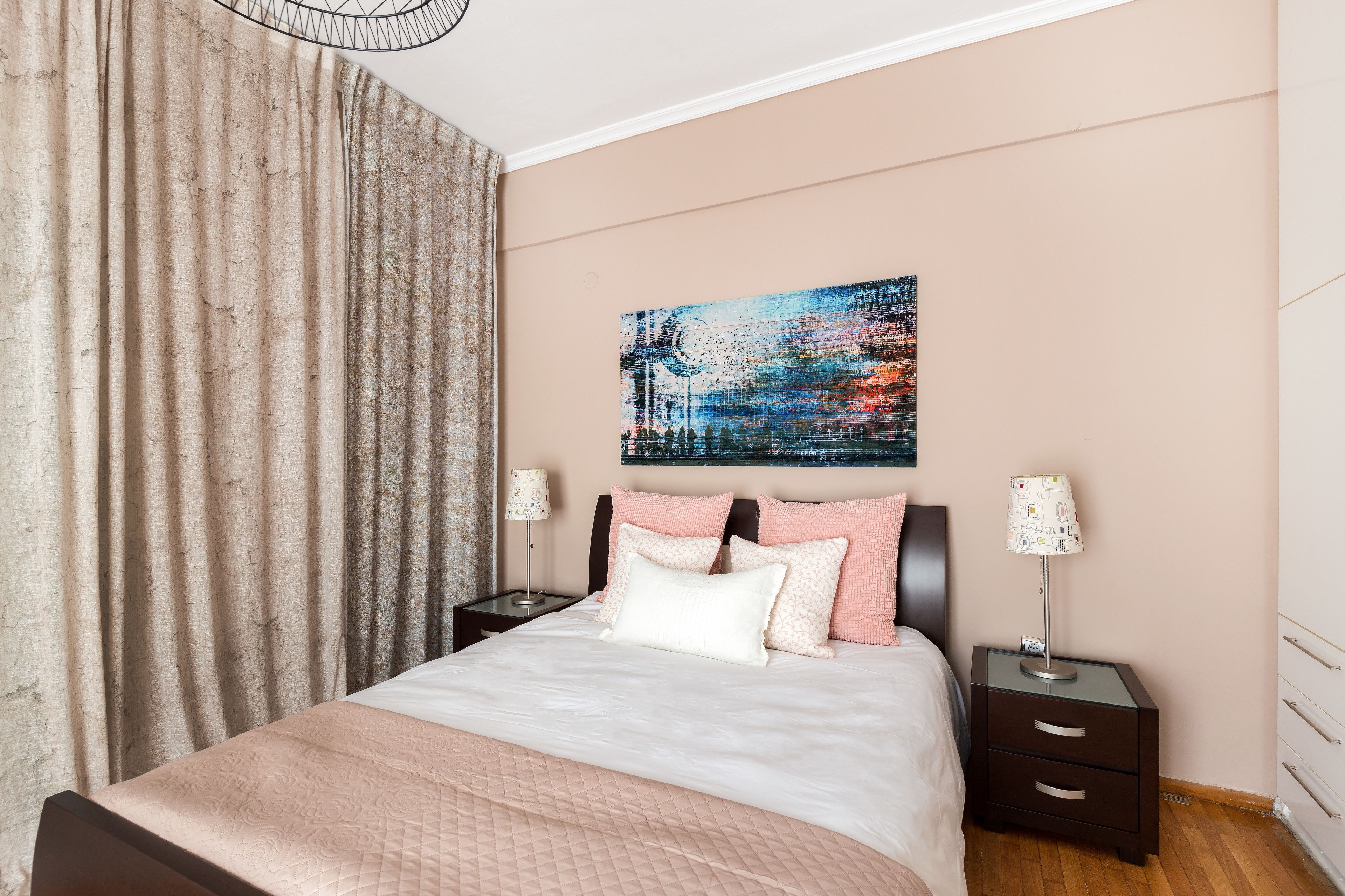 A bedroom with a bed, two bedside tables, a nightstand, a wall-mounted lamp, and a large abstract painting.