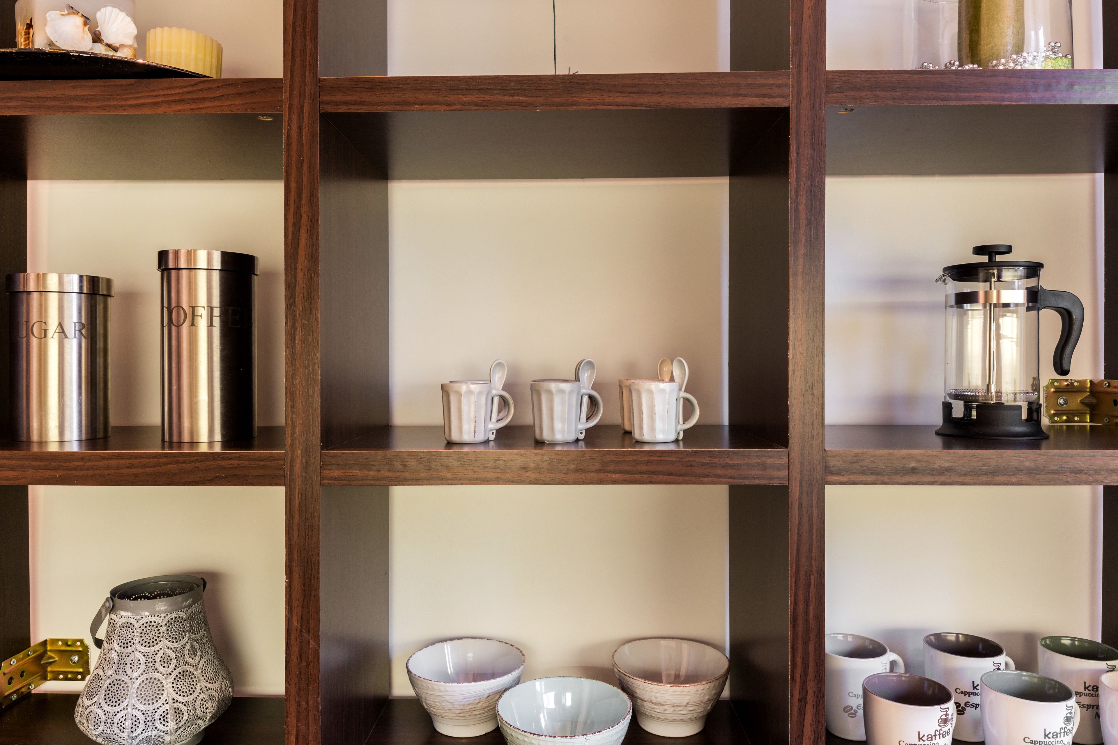 A shelf with various kitchenware items including coffee pots, mugs, and bowls.