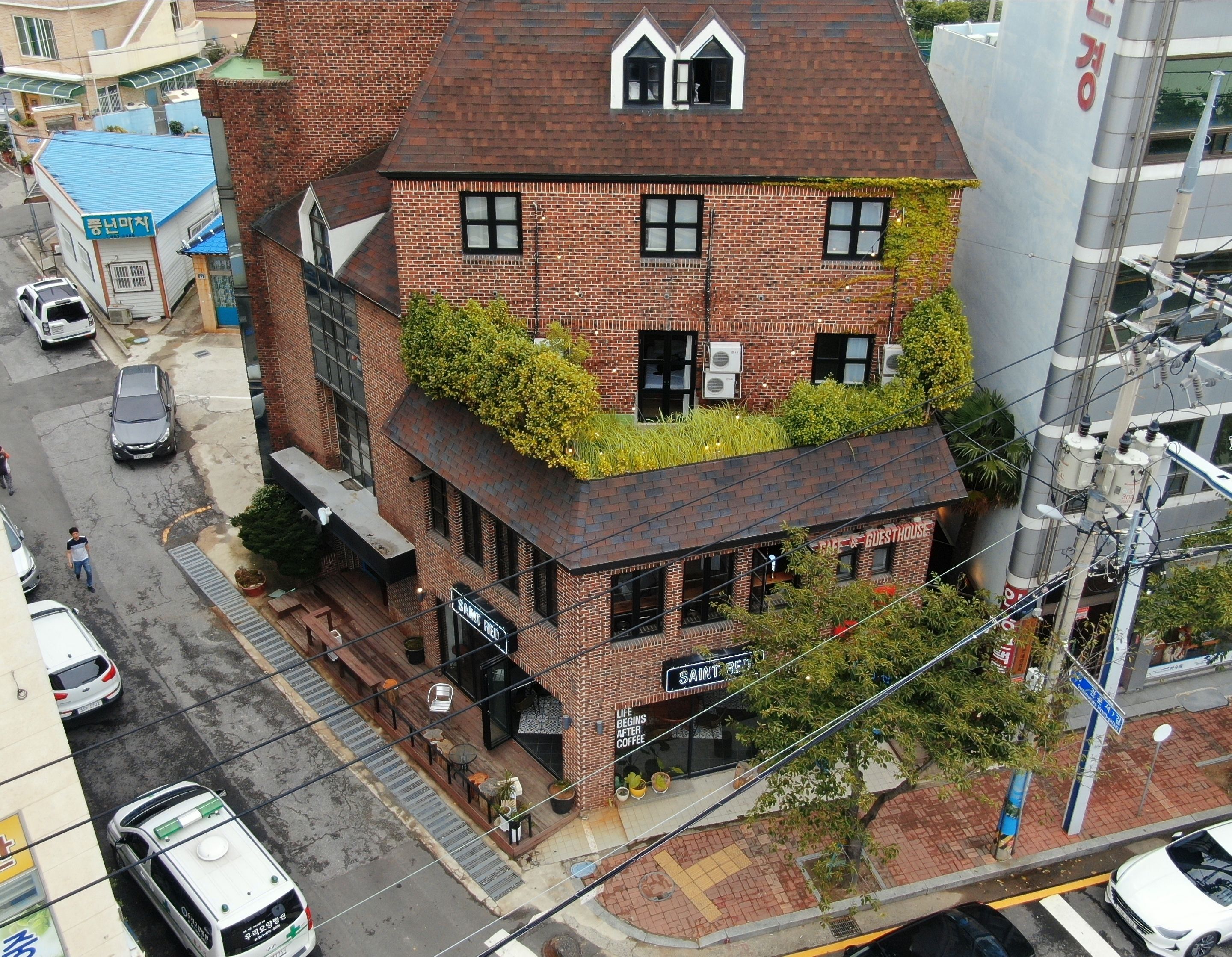 A multi-story building with a brick facade, a rooftop garden, and a ground-level cafe named "SAINT REY."