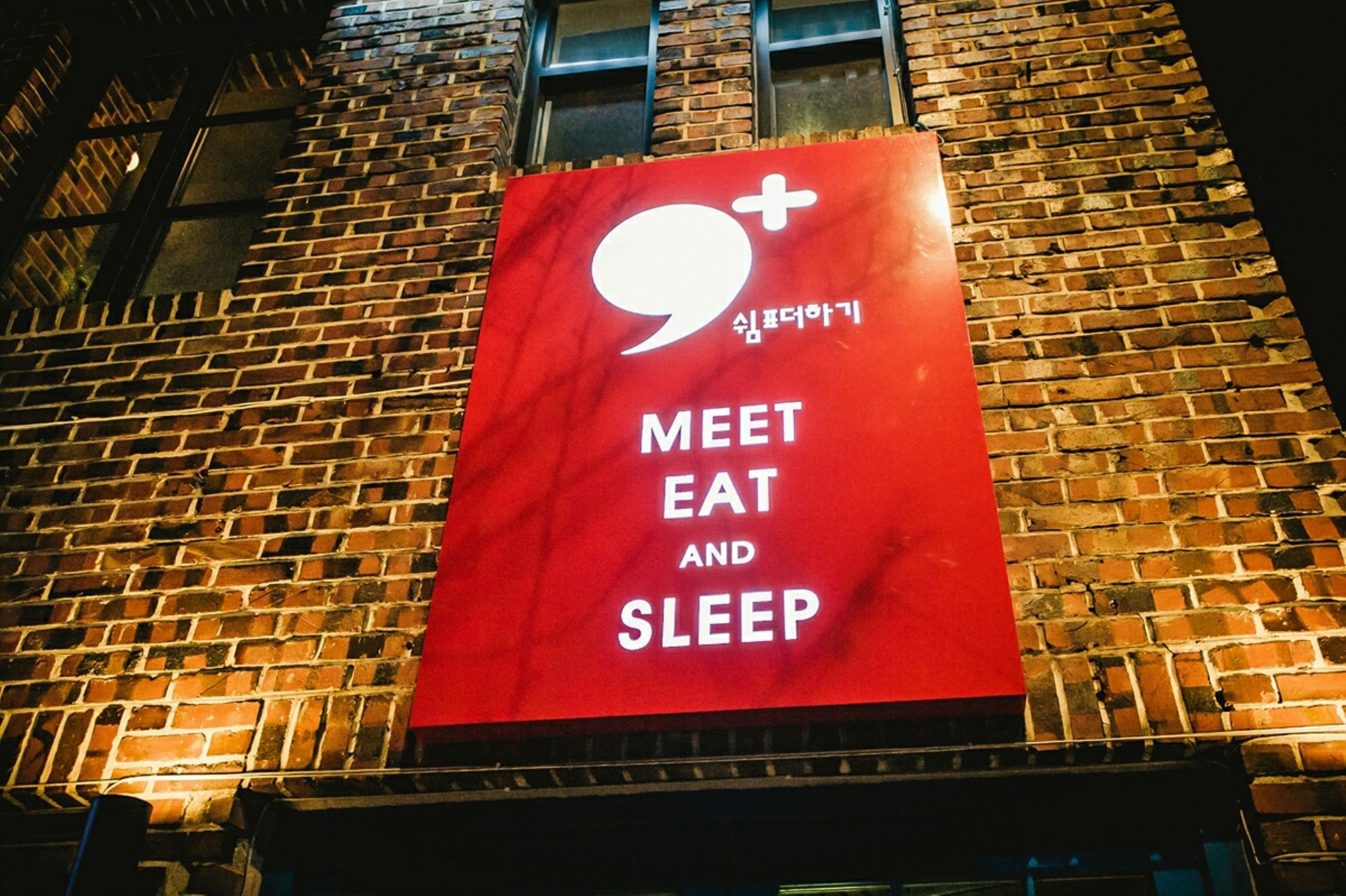 A brick building with a large red sign that reads "MEET EAT AND SLEEP".