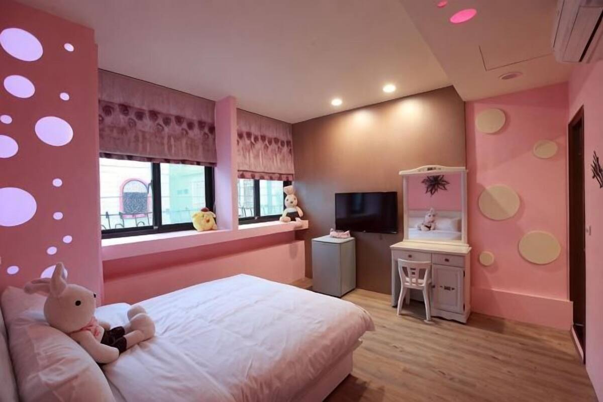A bedroom with a bed, a desk, a chair, a TV, and a window with a view of the outside.