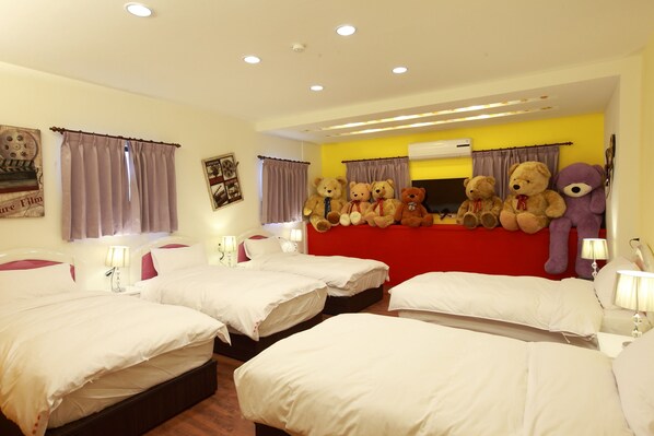 A hotel room with four beds, a red headboard, and multiple teddy bears.