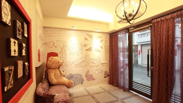 A hotel lobby with a large teddy bear on a bench, a wall with various drawings and text, and a door leading outside. - Fasiter B&B (Hualien City)