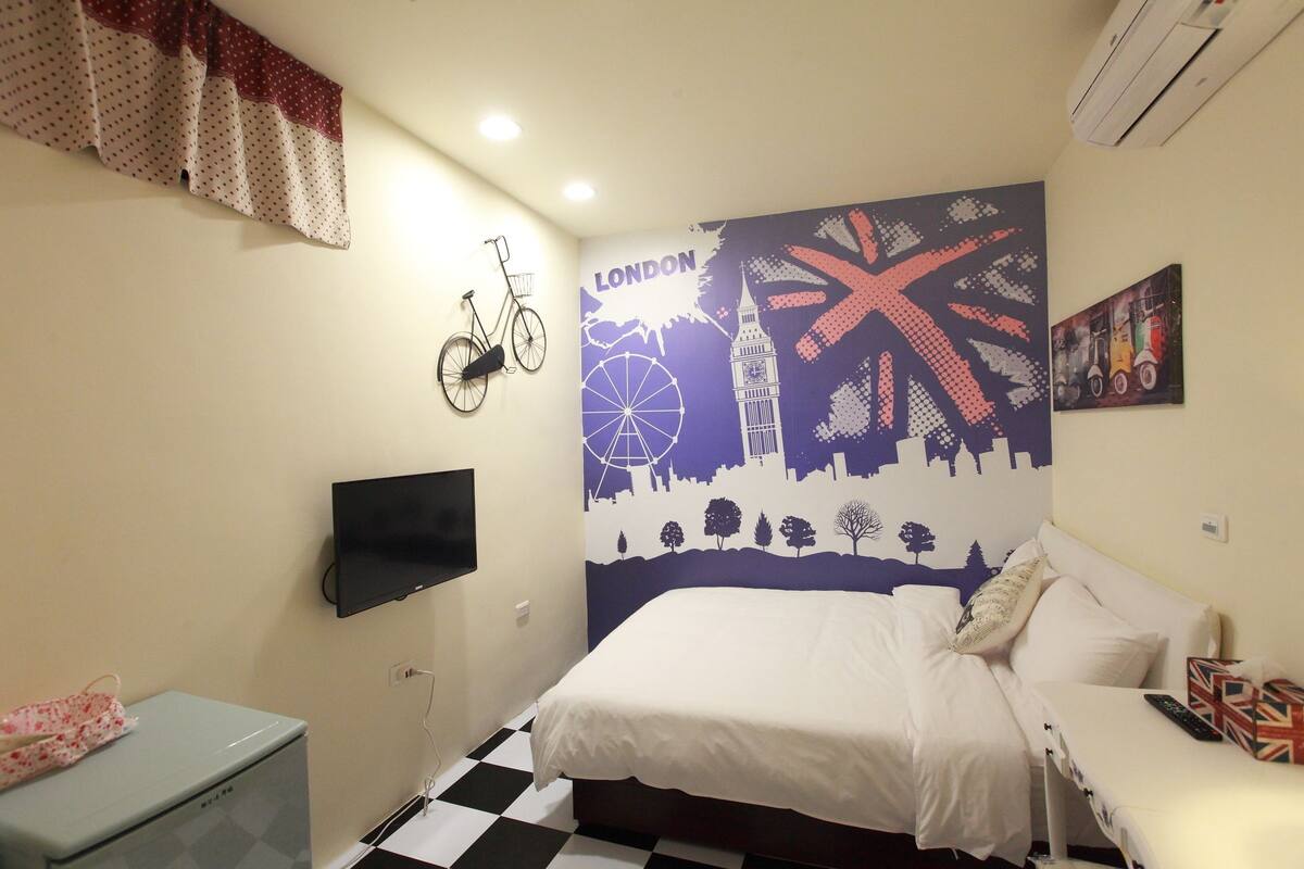 A bedroom with a bed, a TV, a bicycle on the wall, and a wall mural of London landmarks.